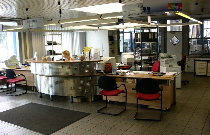 Empfangs- und Service-Annahme des Autozentrum Epple in Rutesheim mit Rundtheke, Mitarbeiterin und Beschilderung ‚Information / Kasse‘