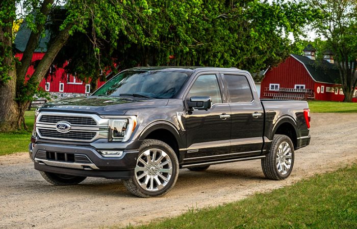 Dunkelgrauer Ford F-150 Pickup auf unbefestigter Landstraße vor roten Scheunen und Bäumen.